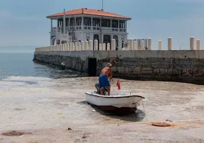 man in motorboat by a pier with the sea surface covered in marine mucilage